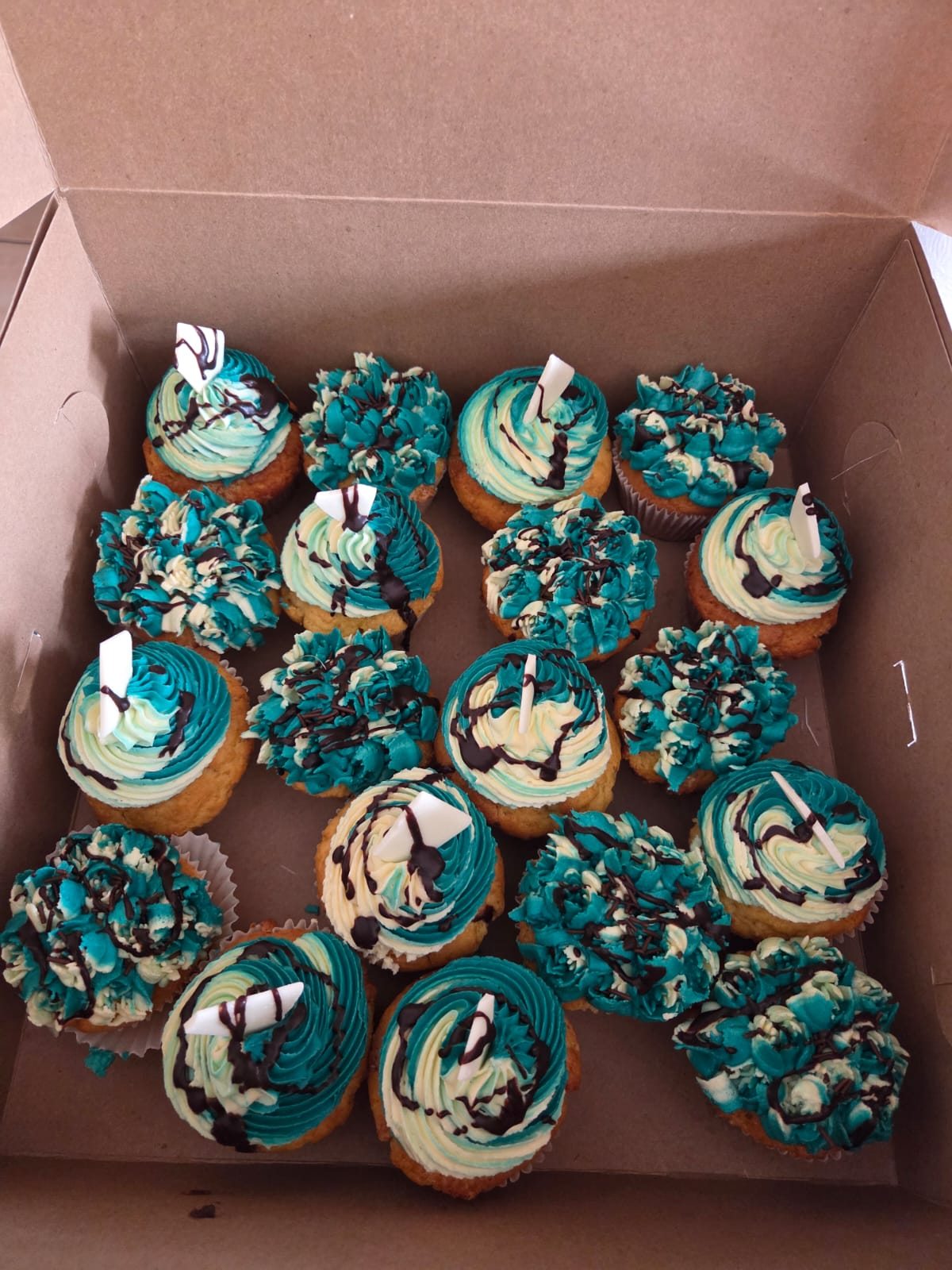 Cupcakes decorated with teal and cream buttercream, chocolate drizzle and white chocolate shards